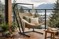 Compact black steel C-frame stand holding a woven hammock chair on a balcony